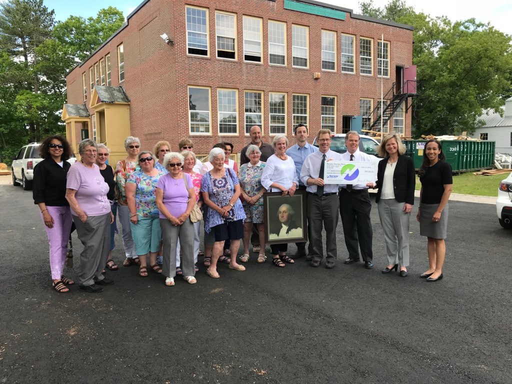 Group of people in front of old school holding check