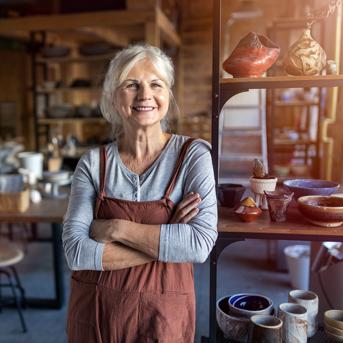 elder woman standing in her pottery studio and smiling because she has a business loan