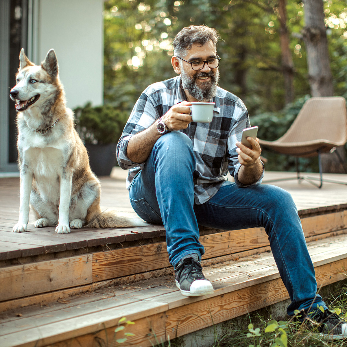 Man sitting on deck step looking at phone and smiling as he learns about home equity