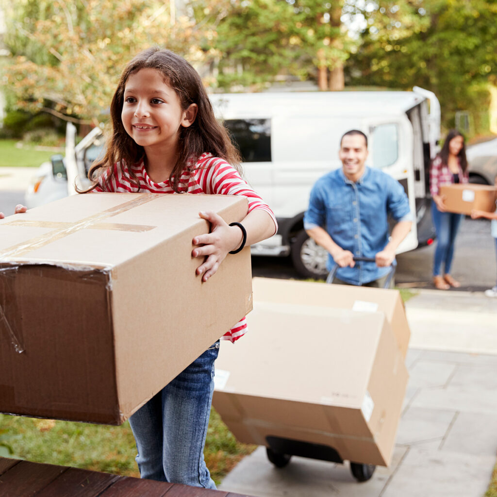 young girl carrying a large moving box into the new home her parents bought with a mortgage
